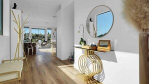 Un interior moderno con suelo de madera, un espejo redondo y un pequeño estante con objetos decorativos.