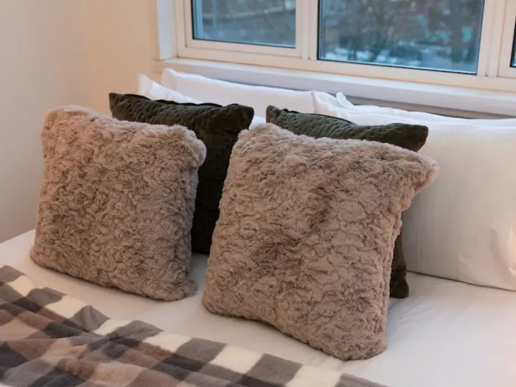 Uma cama com três almofadas fofas e um cobertor xadrez.
