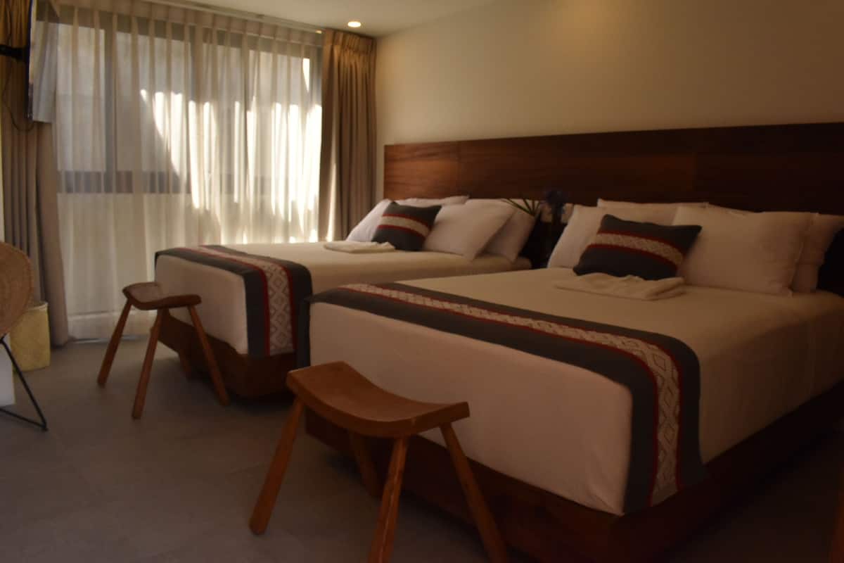 A hotel room with two beds, a wooden stool, and a window with curtains.