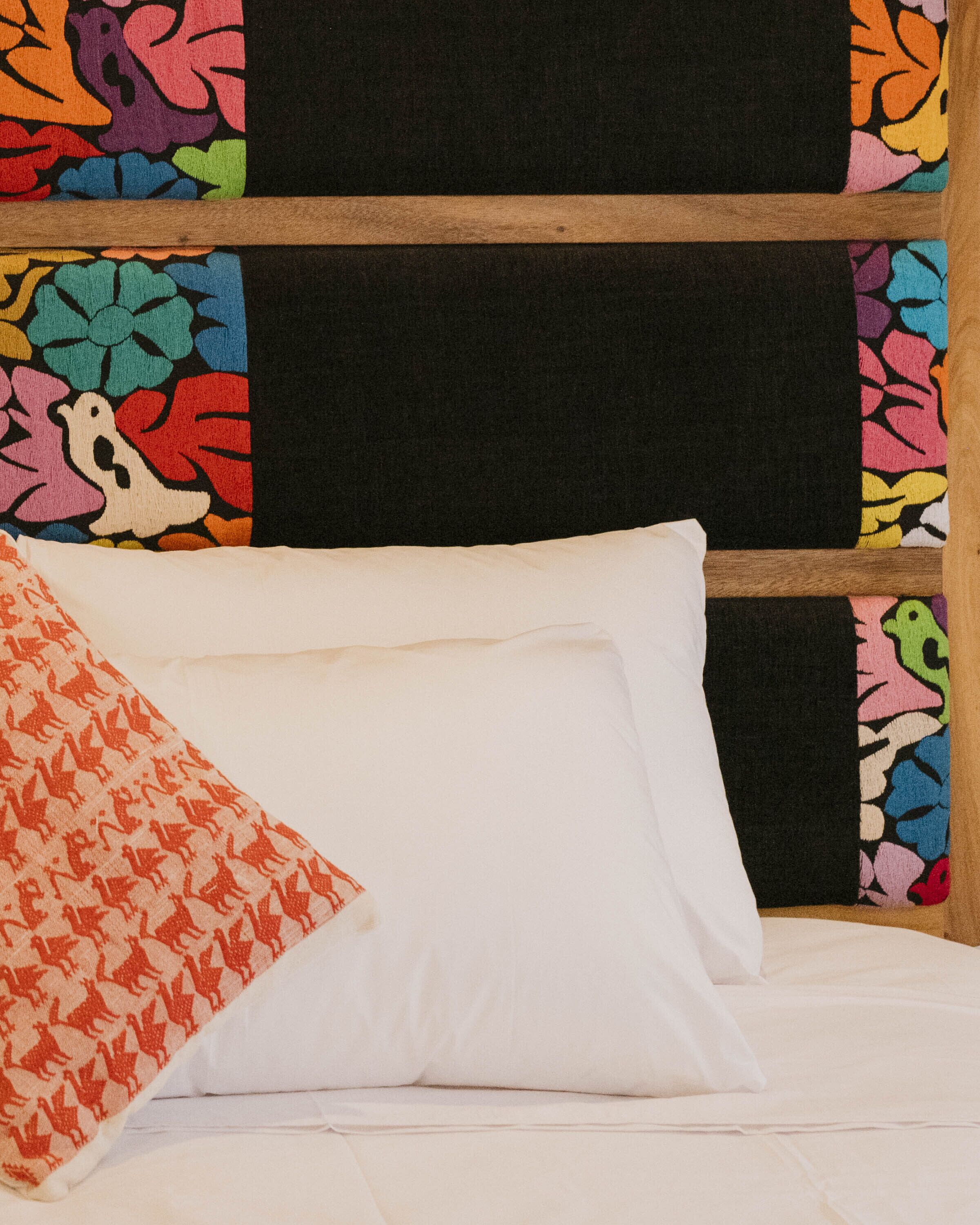 A bed with white linens and a colorful pillow.