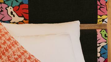 A bed with white linens and a colorful pillow.