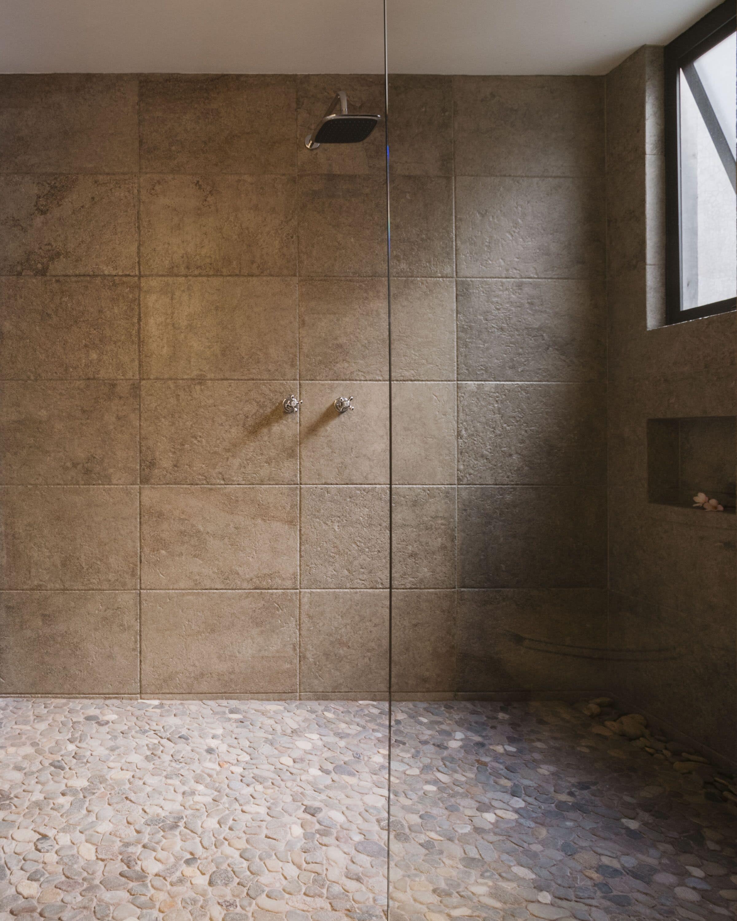 A shower area with stone tiles and a pebble-patterned floor.