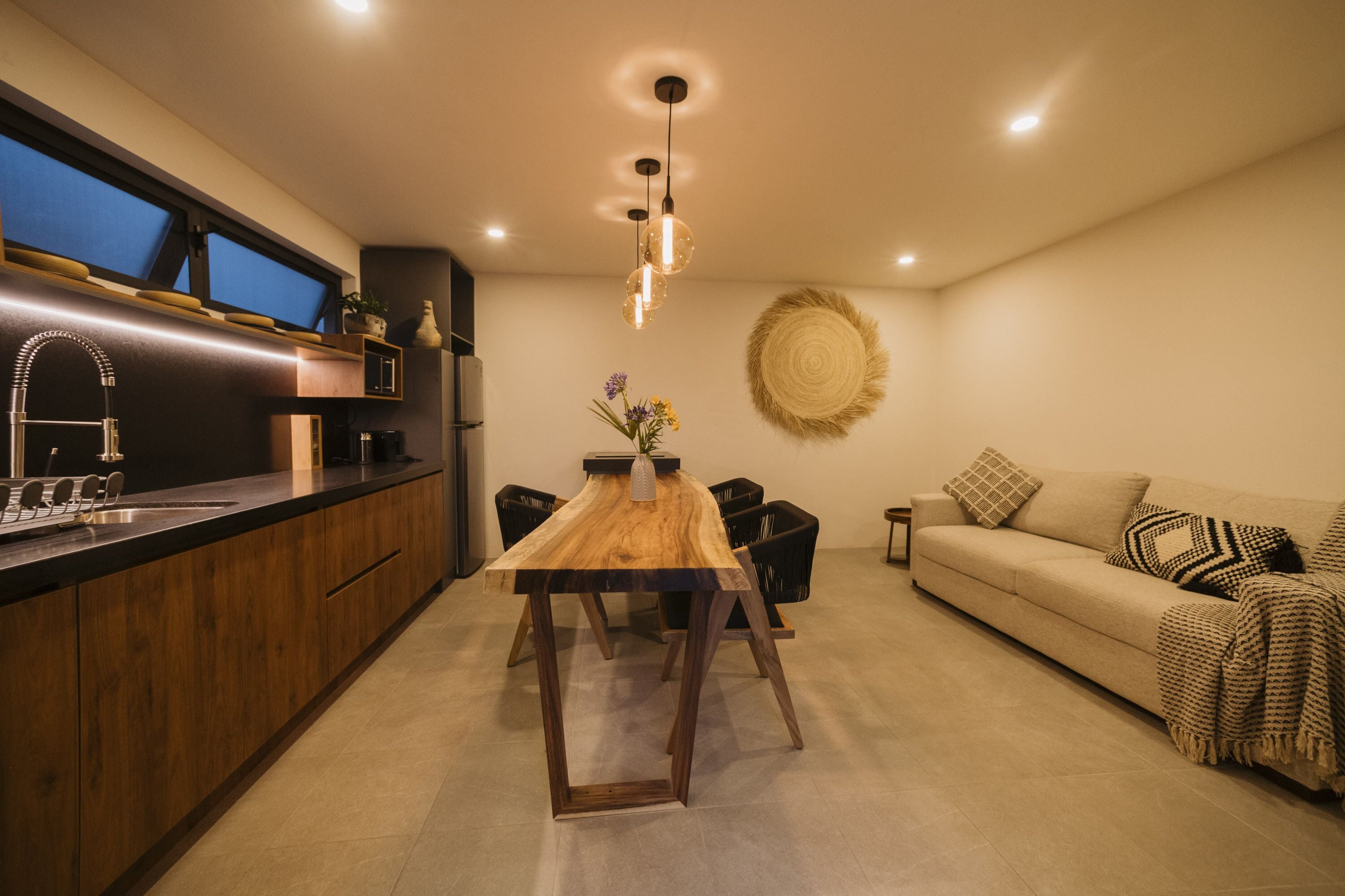 A modern kitchen with a wooden island, a dining area with a table and chairs, and a living area with a sofa and decorative wall art.
