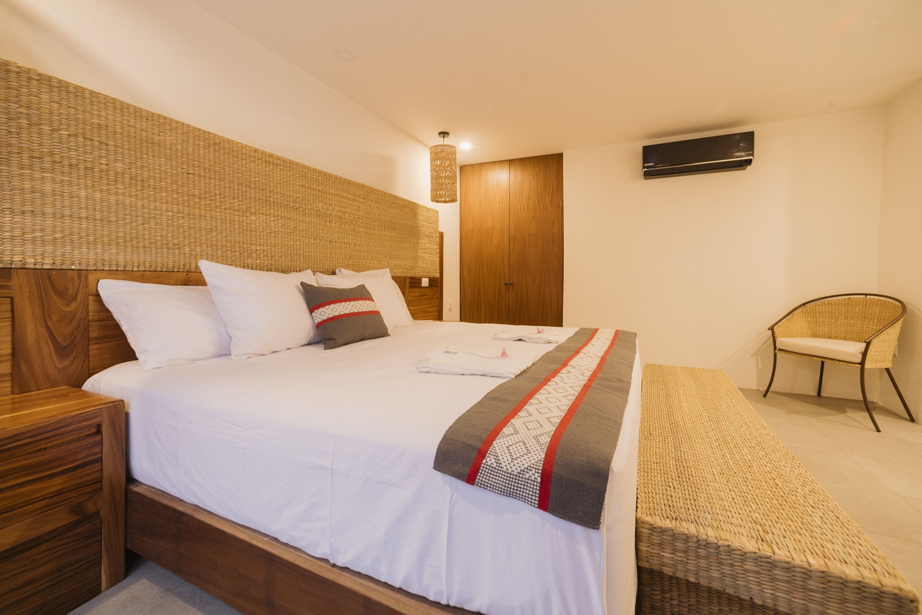A neatly arranged bedroom with a large bed, a wooden headboard, a wicker chair, and a small table.