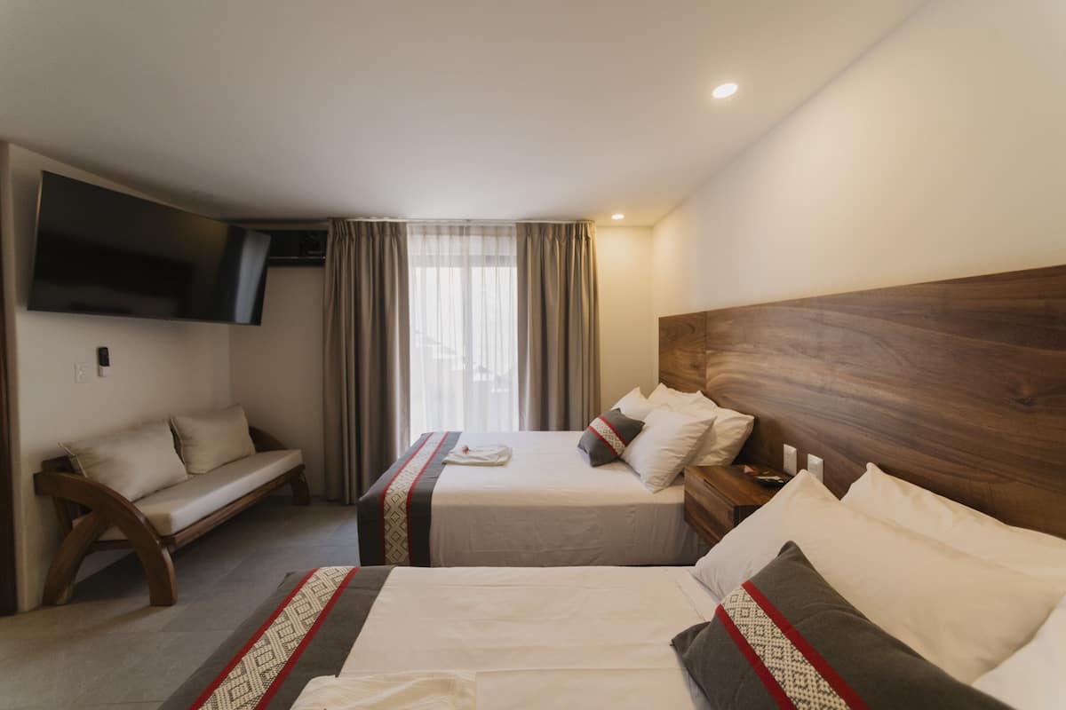 A hotel room with two beds, a sofa, a TV mounted on the wall, and a window with curtains.