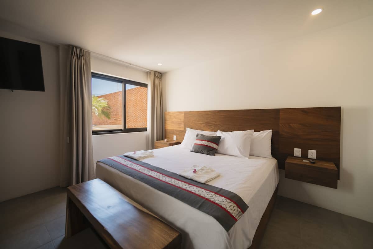 A neatly made bed with a wooden headboard, a bedside table with a lamp, and a window with curtains.