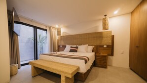 Une chambre moderne avec un grand lit, un banc, une tête de lit en osier et une vue sur l’extérieur grâce à une porte vitrée.
