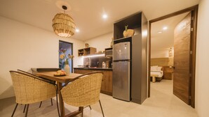 Une cuisine moderne avec une table à manger, des chaises en osier, un réfrigérateur et un luminaire suspendu.