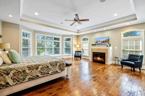 Quarto espaçoso com uma cama grande, lareira, ventilador de teto e várias janelas.