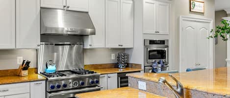 A modern kitchen with white cabinetry, stainless steel appliances, granite countertops, and a built-in oven.