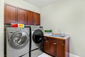 Un espace buanderie compact comprenant un lave-linge et un sèche-linge à chargement frontal, des armoires en bois, un évier et une petite plante en pot.