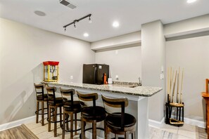 Una cocina con una isla central, taburetes de bar, un refrigerador y un microondas.