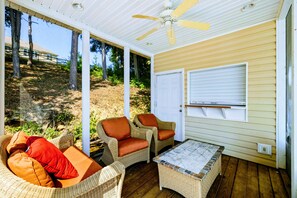 Un espacio de estar techado al aire libre con mobiliario de mimbre y un ventilador de techo.