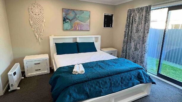 Une chambre à coucher comprenant un lit, des tables de chevet, un radiateur, un tableau décoratif au mur et une fenêtre avec des rideaux.