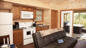 A compact kitchen with wooden cabinets, a white stove, and a microwave. There's a dining area with a brown leather couch and a tablet on it.