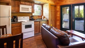 A wooden cabin interior with a kitchen, dining area, and a sofa.