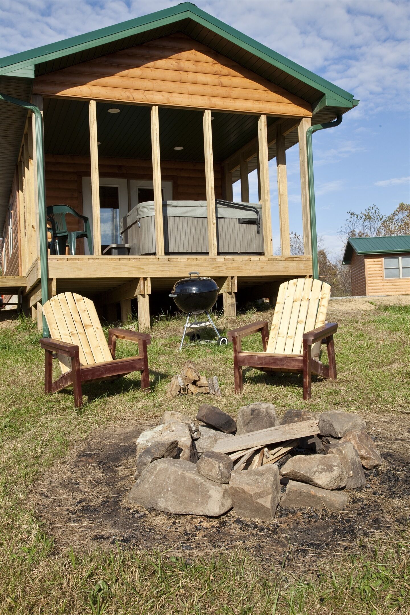 A wooden cabin with a porch, two Adirondack chairs, a grill, and a fire pit.