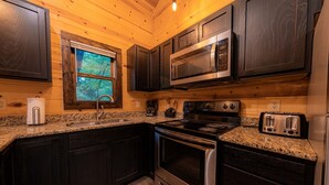 Une cuisine dotée de meubles en bois foncé, de plans de travail en granit, d’appareils électroménagers en acier inoxydable et d’une fenêtre donnant sur les arbres.