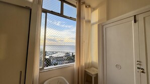 Una habitación con un ventanal grande, una puerta blanca y una pequeña mesa.