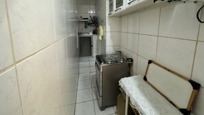 Una cocina compacta con paredes de azulejos blancos, estufa, microondas y un mueble pequeño.