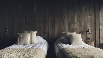 Twee enkele bedden met witte lakens en beige dekens, houten wanden en twee wandlampen.