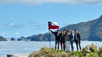 A group of people standing by a body of water with a flag, rocky terrain, and a clear sky.