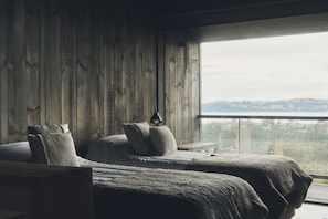 Un dormitorio con un ventanal grande, paredes de madera y dos camas con almohadas.