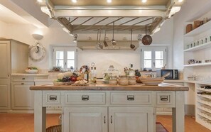 Une cuisine dotée d’un îlot central, de meubles blancs et de casseroles suspendues, ainsi que de divers produits alimentaires disposés sur le plan de travail.