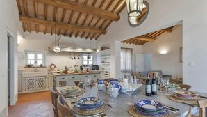 A spacious dining area with a high ceiling and exposed wooden beams, a kitchen in the background, and a dining table set for a meal. - Villa in Magliano In Toscana with 8 bedrooms sleeps 17 (Magliano In Toscana)