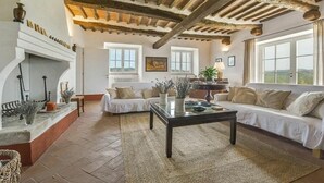 A spacious living room with a fireplace, two sofas, a coffee table, and large windows offering a view. - Villa in Magliano In Toscana with 8 bedrooms sleeps 17 (Magliano In Toscana)