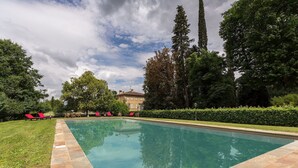 A rectangular swimming pool with a stone border, surrounded by a well-maintained lawn and several red lounge chairs. - Villa in Pisa with 7 bedrooms sleeps 14 (Pisa)