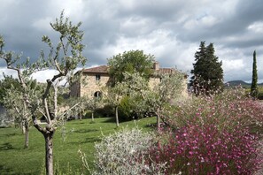 A stone building with a tiled roof, surrounded by a well-maintained garden with various plants and flowers.
