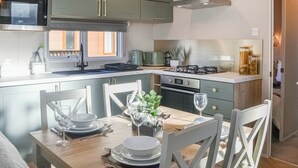 A modern kitchen with green cabinets, a microwave, a stove, and a dining area set with white chairs and plates. - Waterfoot Lodge (W09) (Amotherby)