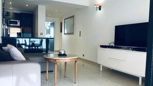 Een moderne woonkamer met een witte bank, een ronde salontafel, een flatscreen televisie en een witte kast.