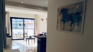Een moderne woonkamer met een glazen deur naar een balkon, een eethoek met een tafel en stoelen, en een keuken met een aanrecht.