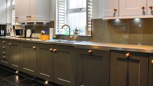 A modern kitchen with a long countertop, built-in appliances, and a window with shutters.