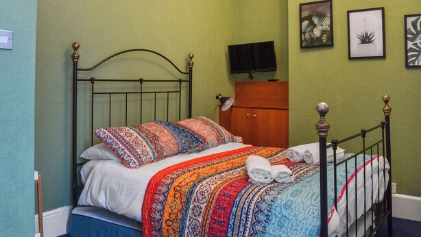 A neatly made bed with patterned bedding, a television on a wooden cabinet, and framed artwork on the wall.