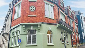 A corner building with a red brick facade, white window shutters, and a green-painted section.