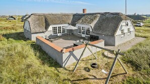 Une maison à toit de chaume avec un patio, une balançoire et une voiture au loin.