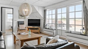 Un salon spacieux avec une grande télévision, des meubles en bois et une vue sur l’extérieur.