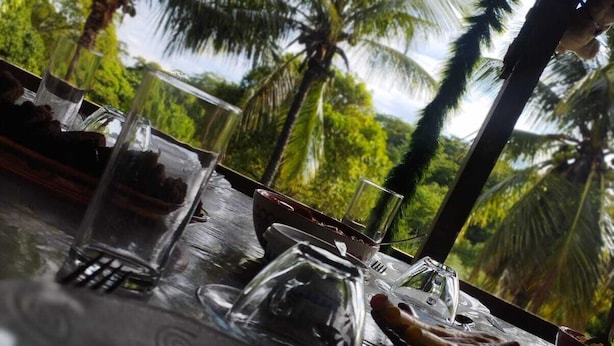 A table set for dining with clear glassware and a tropical backdrop of palm trees. - POUSADA VALE ENCANTADO MACAÉ (Macaé)