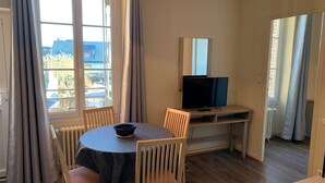 Una habitación con una mesa de comedor, sillas, televisor y una ventana con cortinas.