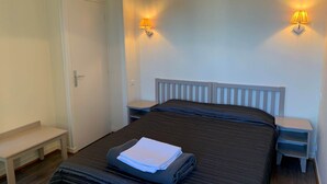 Un dormitorio con cama, mesitas de noche, un banco y lámparas fijadas a la pared.