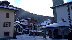 Ein verschneites Dorf mit traditionellen Gebäuden, einem Kirchturm und einem Berg im Hintergrund.