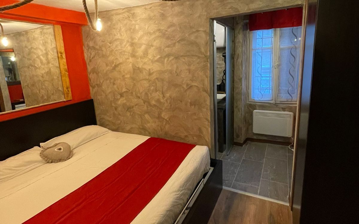 A bedroom with a bed, a red and white striped bedspread, a mirror, and a textured wall.