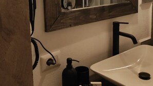 Ein Badezimmer mit einem weißen Waschbecken, einem schwarzen Wasserhahn, einem Spiegel mit Holzrahmen und einer schwarzen Flasche auf der Ablagefläche.