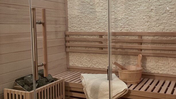 Un sauna avec des bancs en bois, une porte en verre, un seau en bois et un mur en pierre.