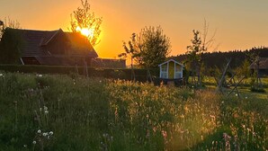 Un paysage rural avec une petite maison en bois et une remise, au coucher du soleil.