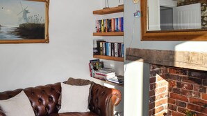 Un salon avec un canapé en cuir marron, une bibliothèque remplie de livres, un tableau encadré et une cheminée en briques.