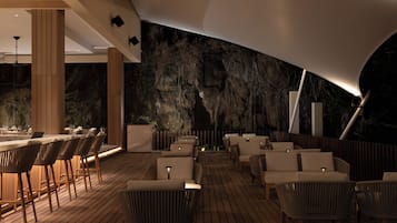An outdoor seating area with wooden flooring, white cushioned chairs, and a bar with stools.